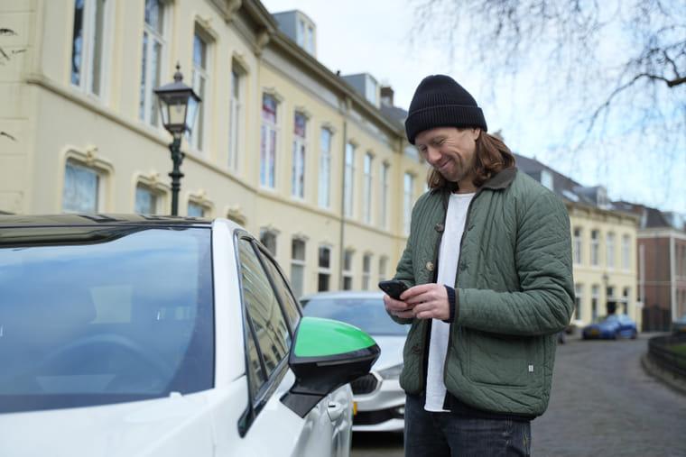 Man gebruikt een deelauto door met de app op zijn telefoon de auto te huren.