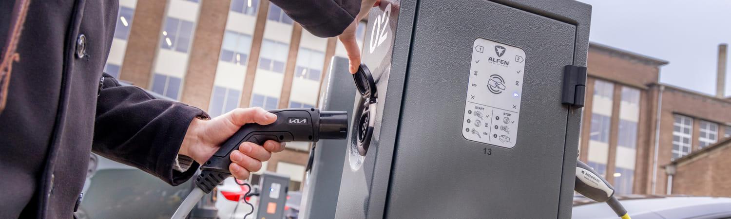 Man steekt stekker in elektrische laadpaal.