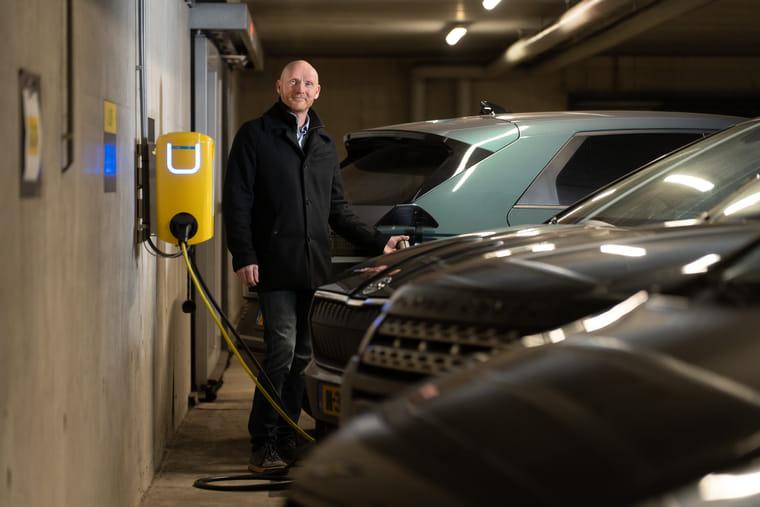 Man staat in de parkeergarage en steekt de stekker van de laadpaal in zijn elektrische auto.