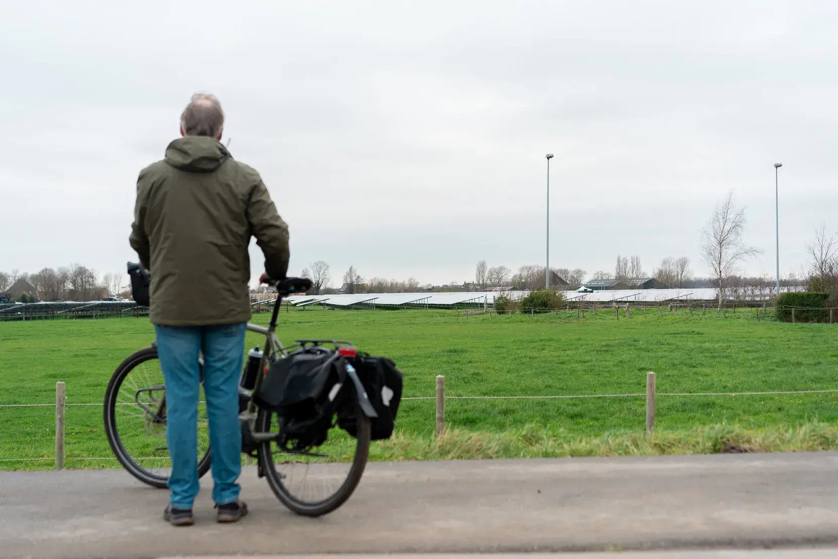 Man staat naast zijn fiets en kijkt naar de zonnepanelen op het boeren land.