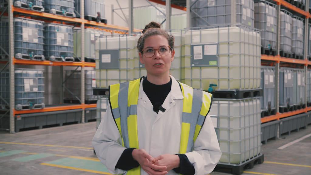 Vrouw geeft uitleg over de processen in de azijnfabriek. Ze draagt een veiligheidshesje.