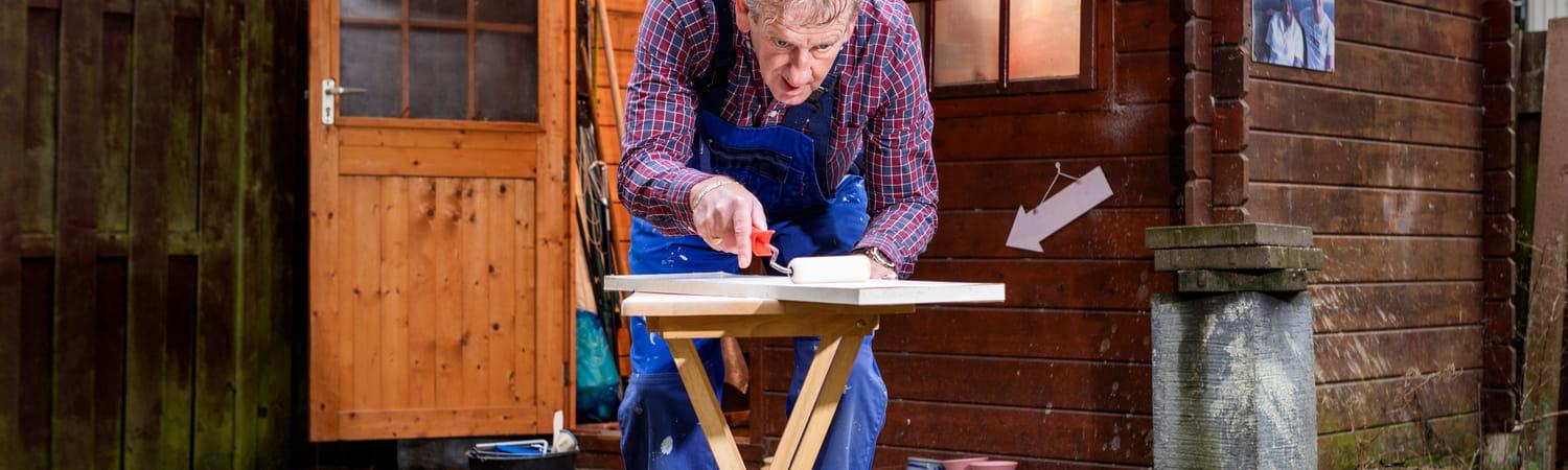Man staat voor zijn schuur een is op een kleine werktafel aan het klussen.