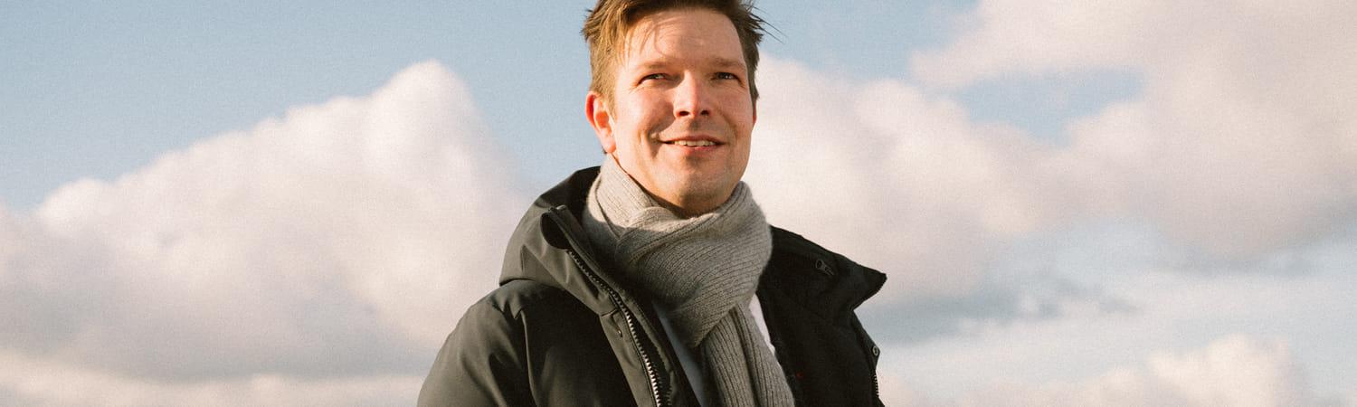 Man in zwarte jas en sjaal poseert voor zonnepanelen.