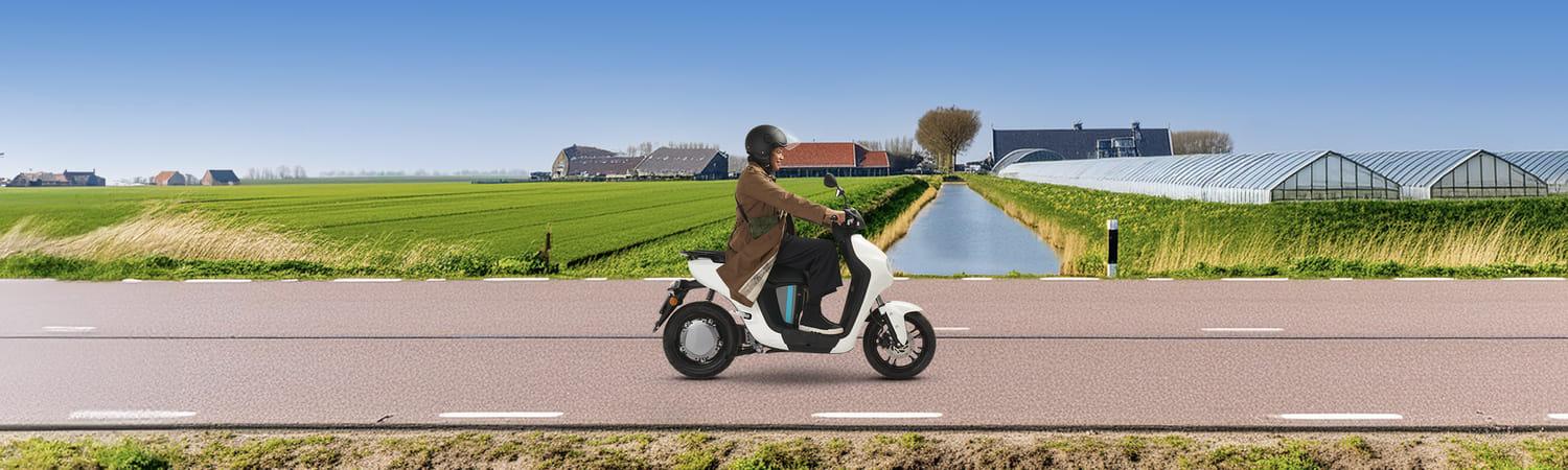 Een vrouw zit op een e-scooter en rijdt door de polder op een weg. Op de achtergrond zie je kassen, een huis en boerderij.