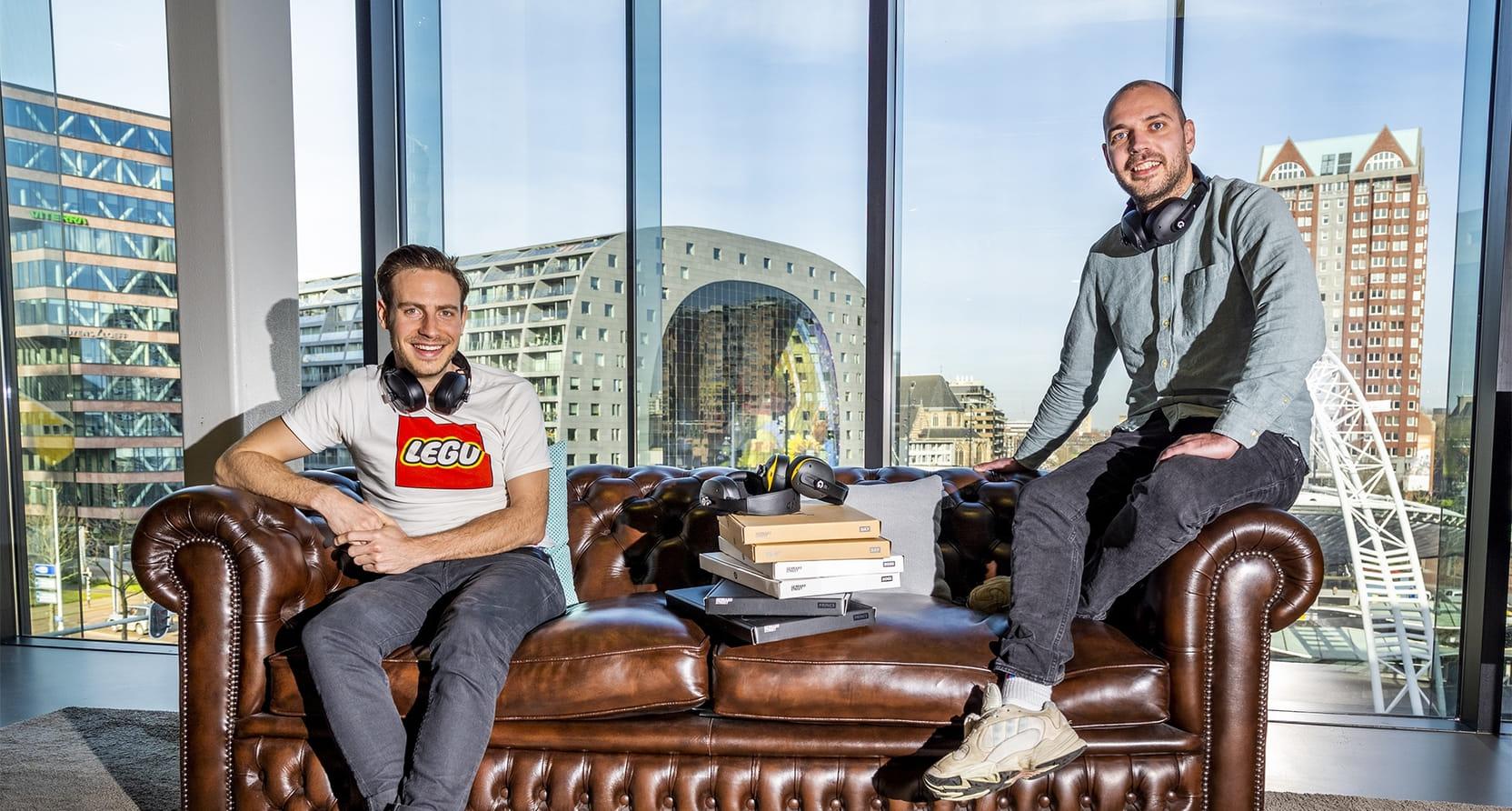 De twee founders van Repeat zitten op een leren bank. Op de bank liggen hun koptelefoons. Ook dragen ze beiden een koptelefoon om hun nek. Op de achtergrond, door het glas, zie je de stad.