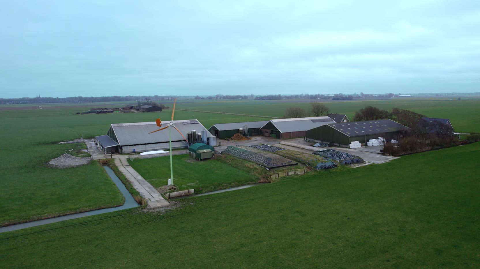 Luchtfoto van een boerenbedrijf in gemeente Koggeland. Je ziet onder andere een kleine windturbine op het erf.