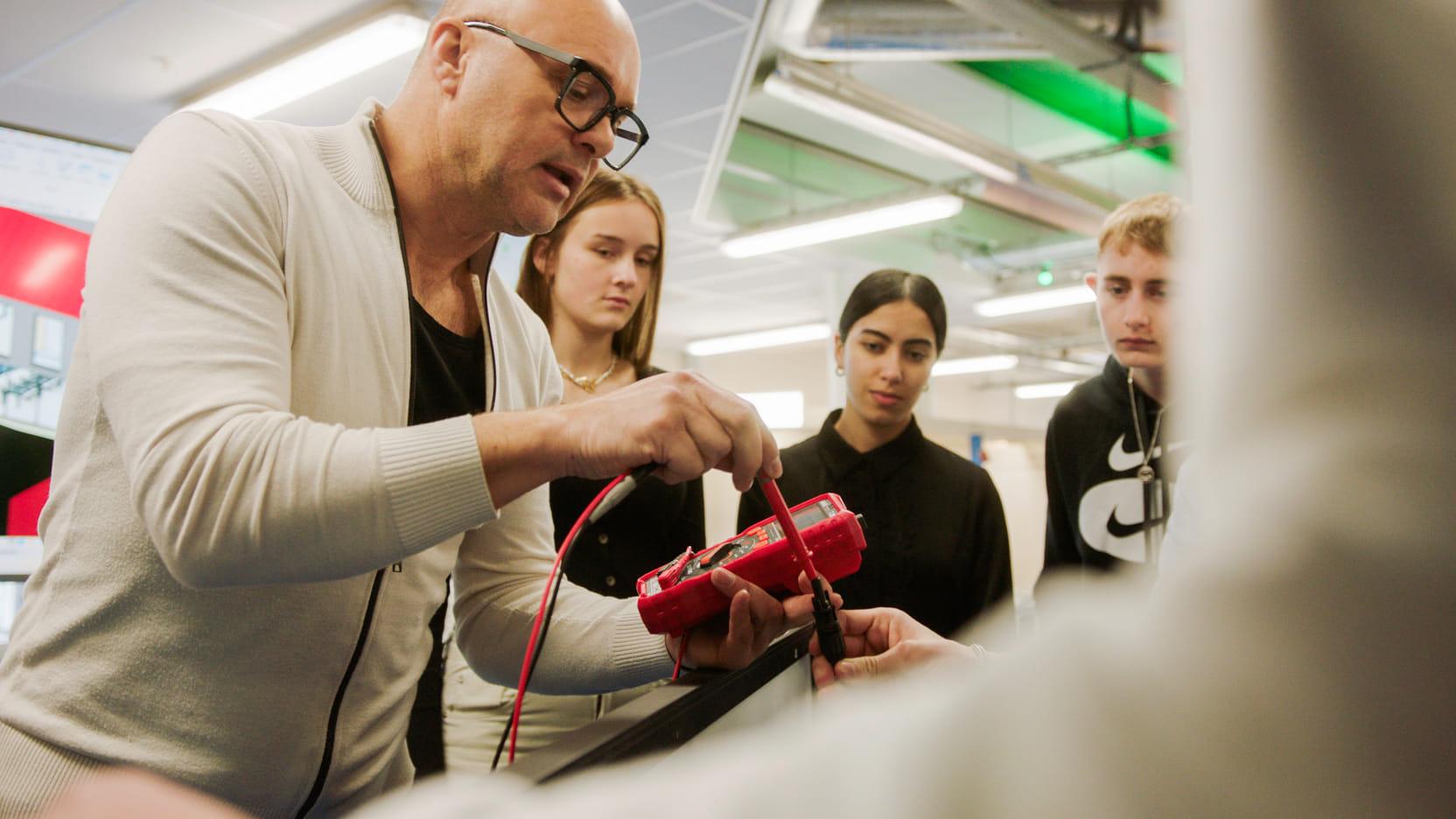 Een docent van het ROC Horizon College in Hoorn geeft studenten les in Smart Building. De studenten kijken hoe hij bezig is met een elektriciteitskabel.