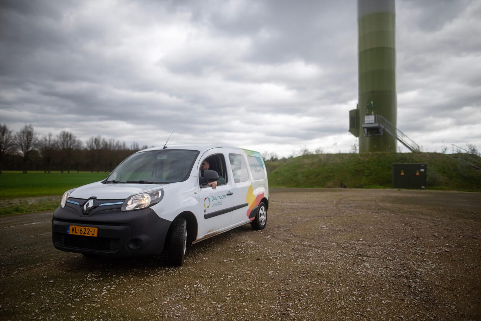 Het busje van Duurzaam Leudal staat op een parkeerterrein voor een windmolen.