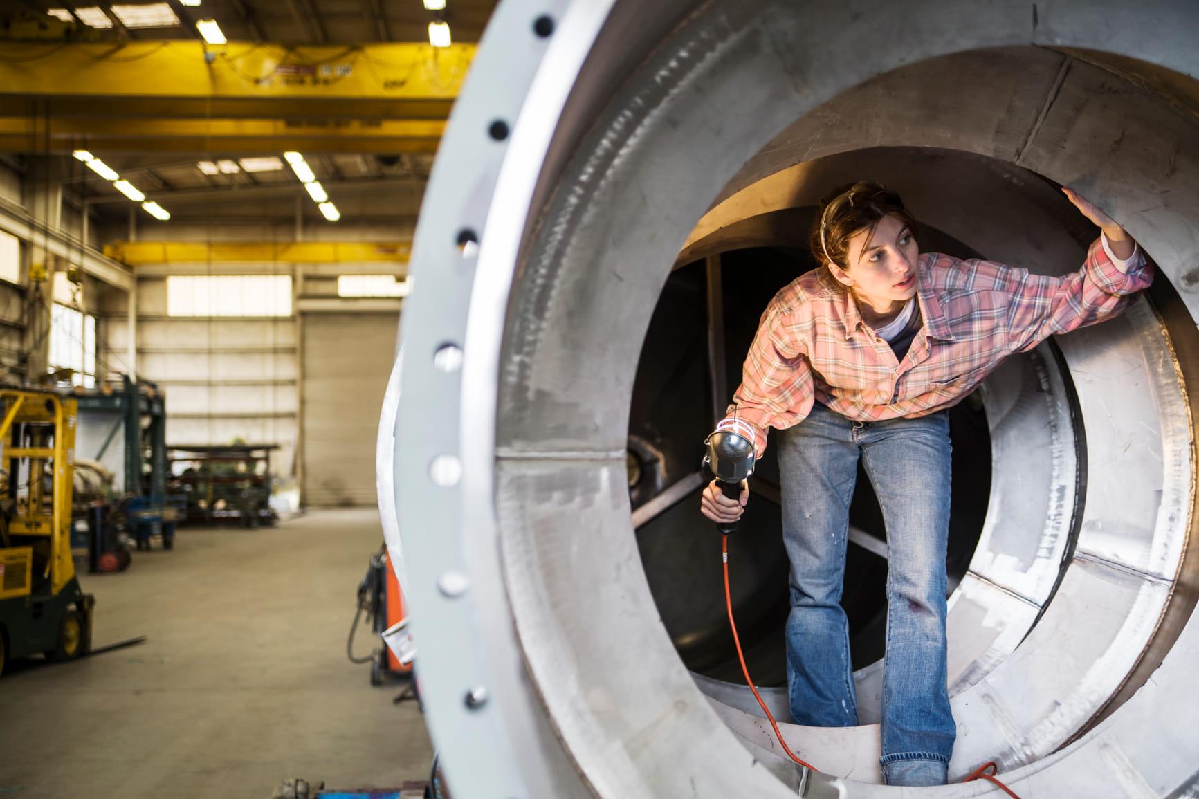 Vrouw in een fabriek loopt door een tunnelvormig voorwerp en inspecteert.