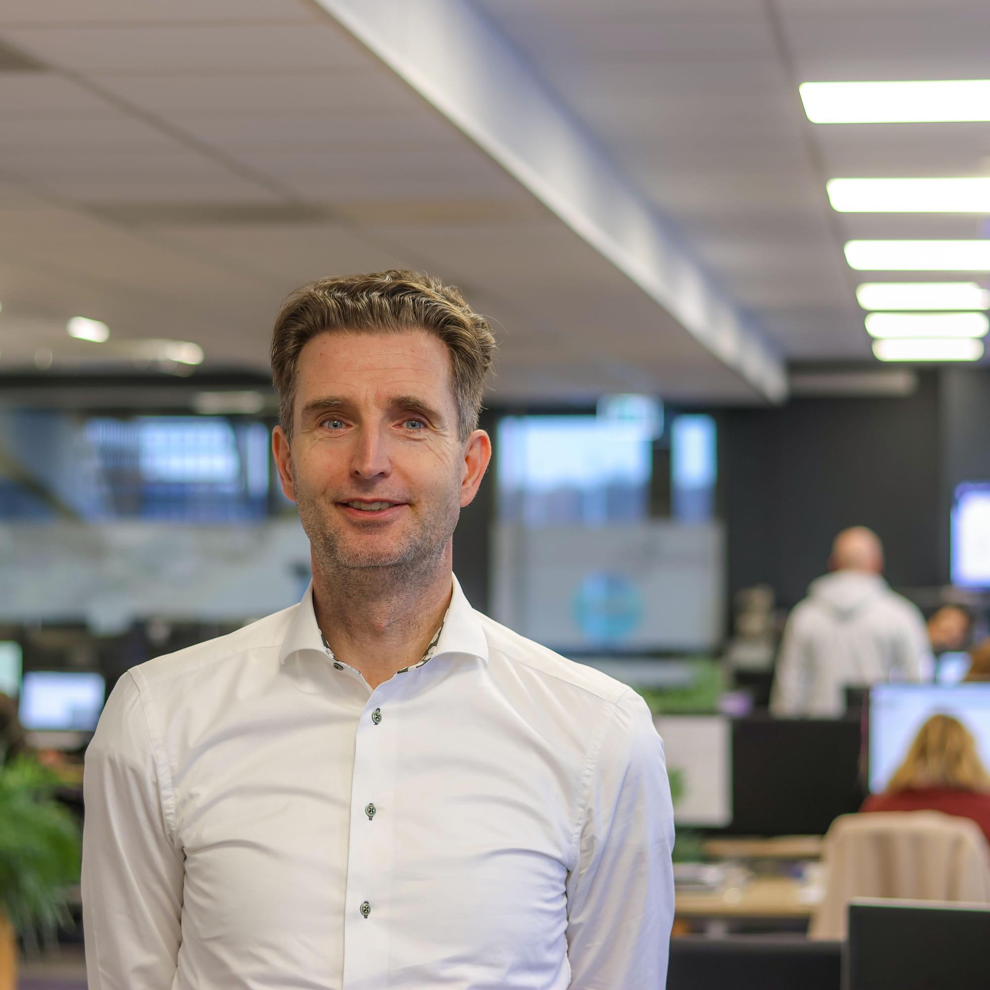 Portret van Caspar Botter, commercieel eindverantwoordelijke bij JC-Electronics. Hij staat in een kantoor en draagt een witte blouse.