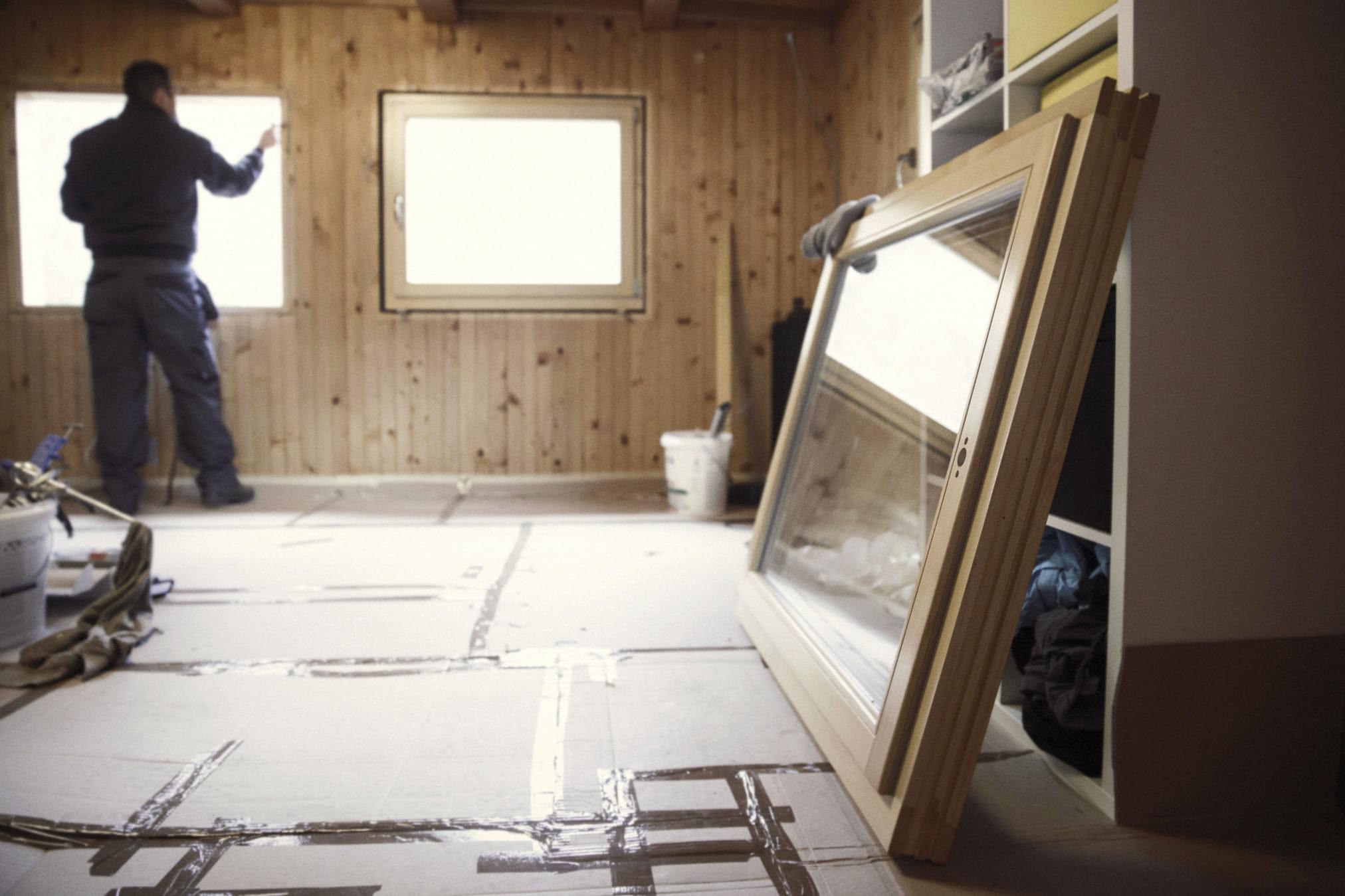 Je ziet dat een man isolatieglas plaatst in een zolderkamer. Op de voorgrond staat nog een los kozijn met het isolatieglas.