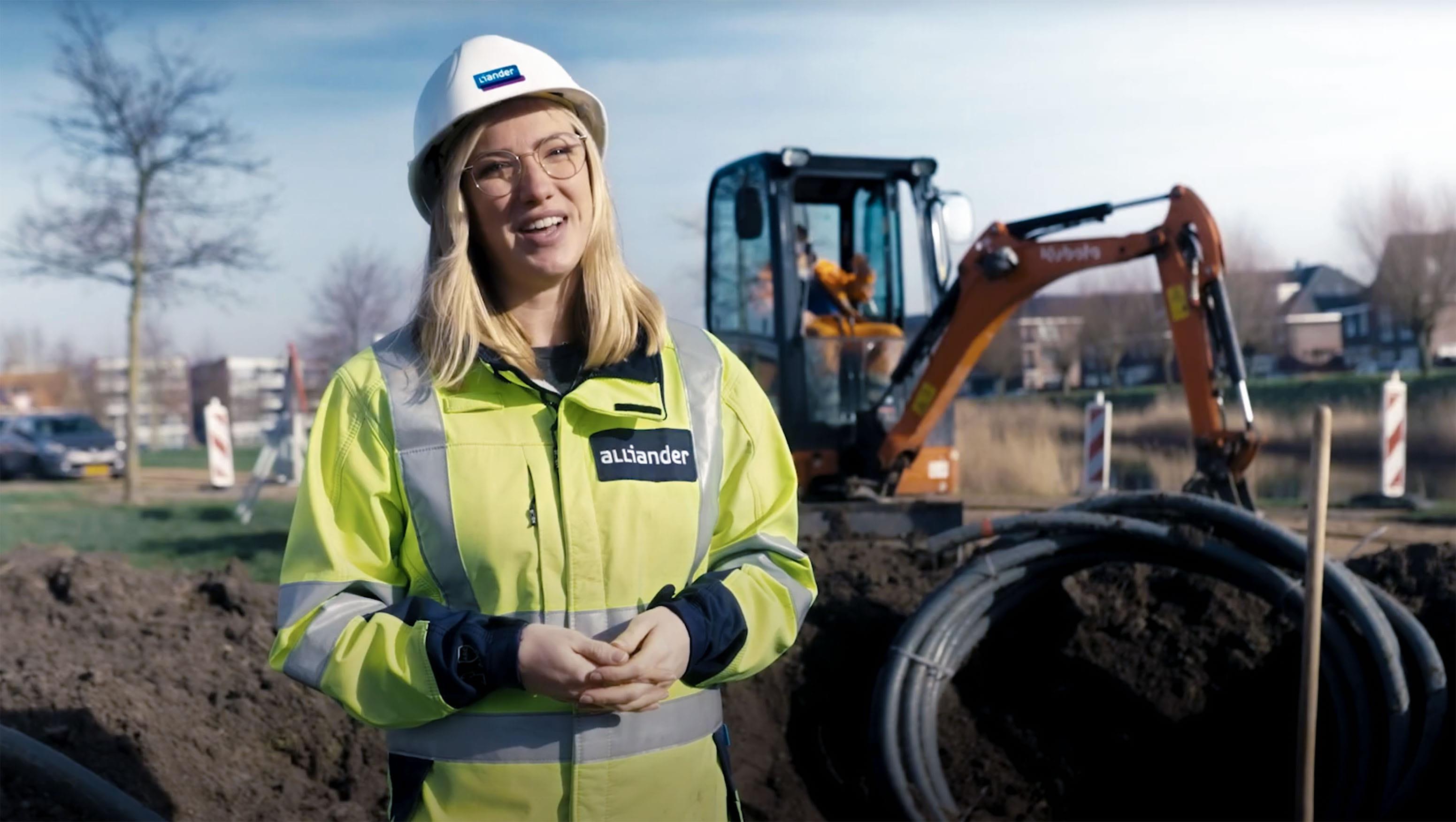 Een medewerker van netbeheerder Liander staat voor een plek waar gewerkt wordt een versterking van het stroomnet. Ze draagt veiligheidspak.