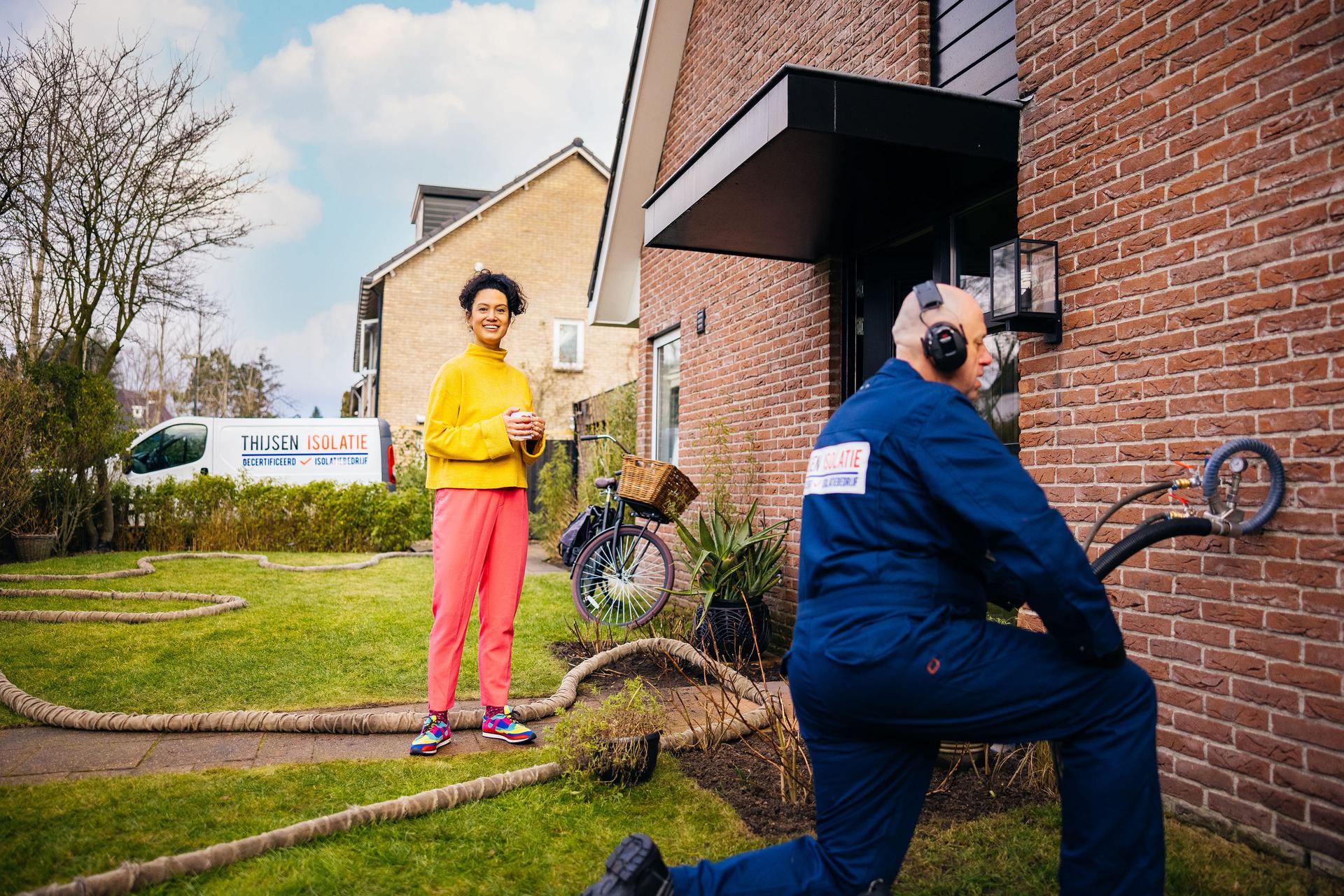 Vrolijke vrouw kijkt toe hoe een man de buitenmuur aan het isoleren is.