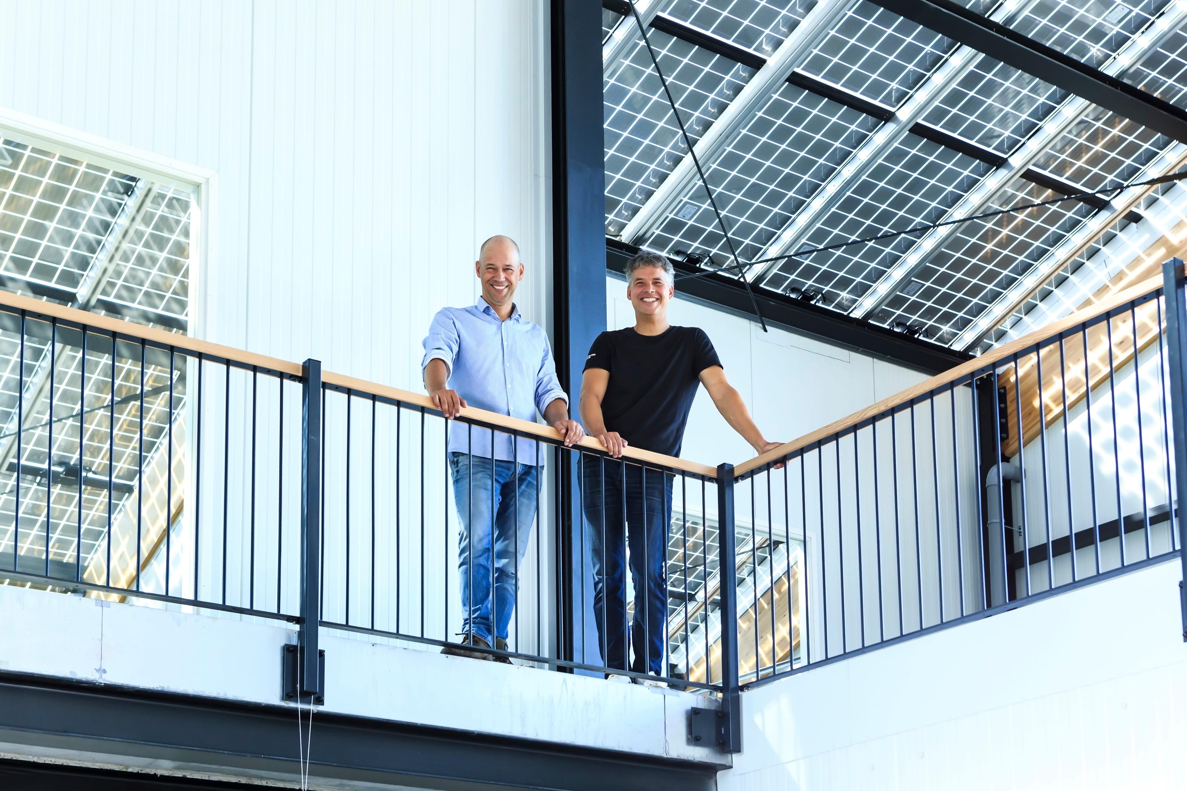 Twee mannen aan een platform met leuning kijken naar beneden en lachen.