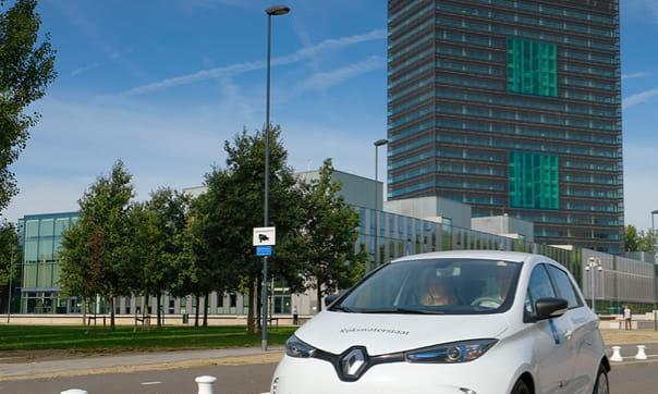 Foto van witte auto die voor een ministeriegebouw wegrijdt.
