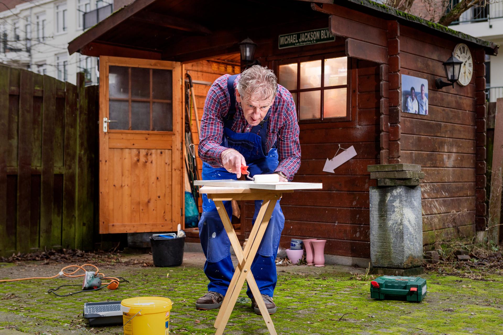 Man staat voor zijn schuur een is op een kleine werktafel aan het klussen.