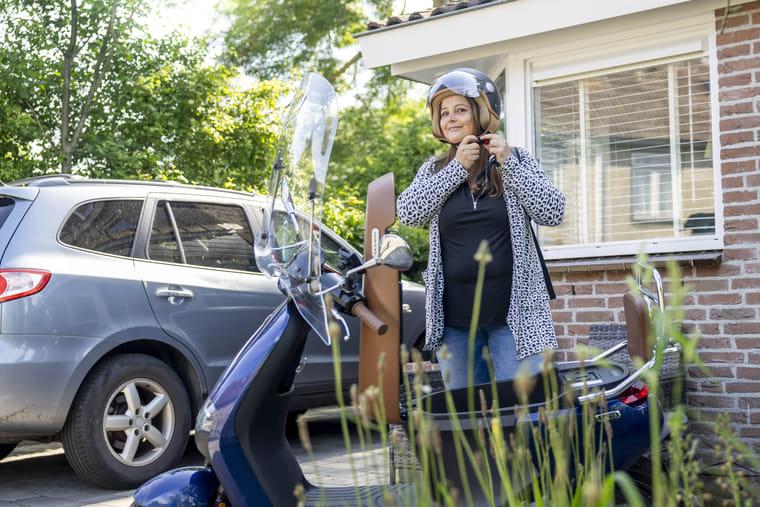 Renate doet haar helm op en maakt zich voor haar huis klaar voor een rit op de e-scooter.