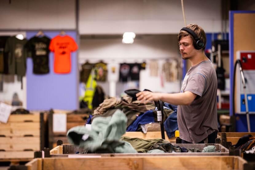 Een man draagt een koptelefoon en is kleding aan het sorteren.