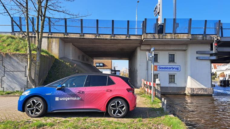 Elektrische deelauto met bedrijfslogo staat geparkeerd naast het water.