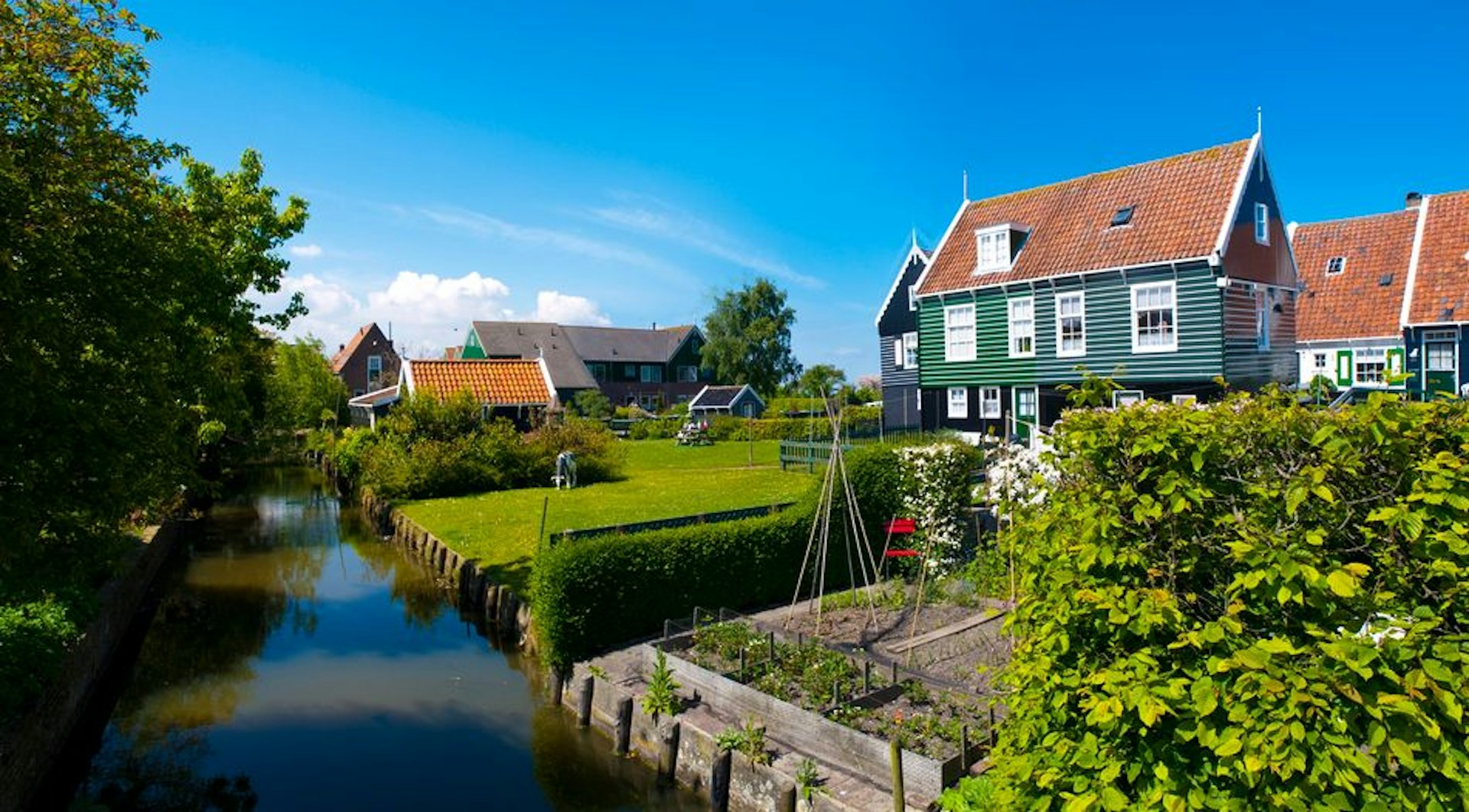 Zonnige foto van een typisch Nederlands huis met grote achtertuin die grenst aan een rivier.