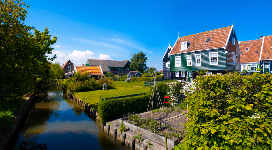 Zonnige foto van een typisch Nederlands huis met grote achtertuin die grenst aan een rivier.