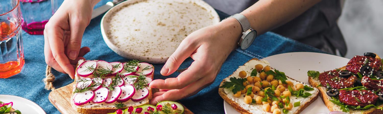 Tafel gevuld met vegetarische gerechten, zoals boterhammen met hummus en radijsjes, komkommer en granaatsappelpitjes.