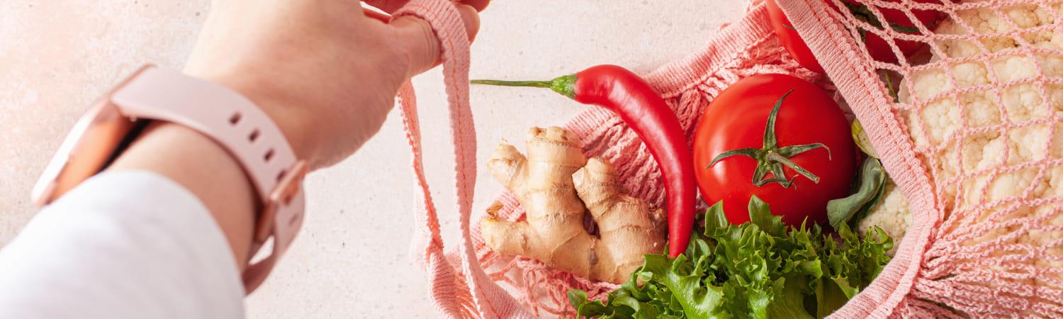 Vrouwenhand houdt een herbruikbare tas vast gevuld met groenten.