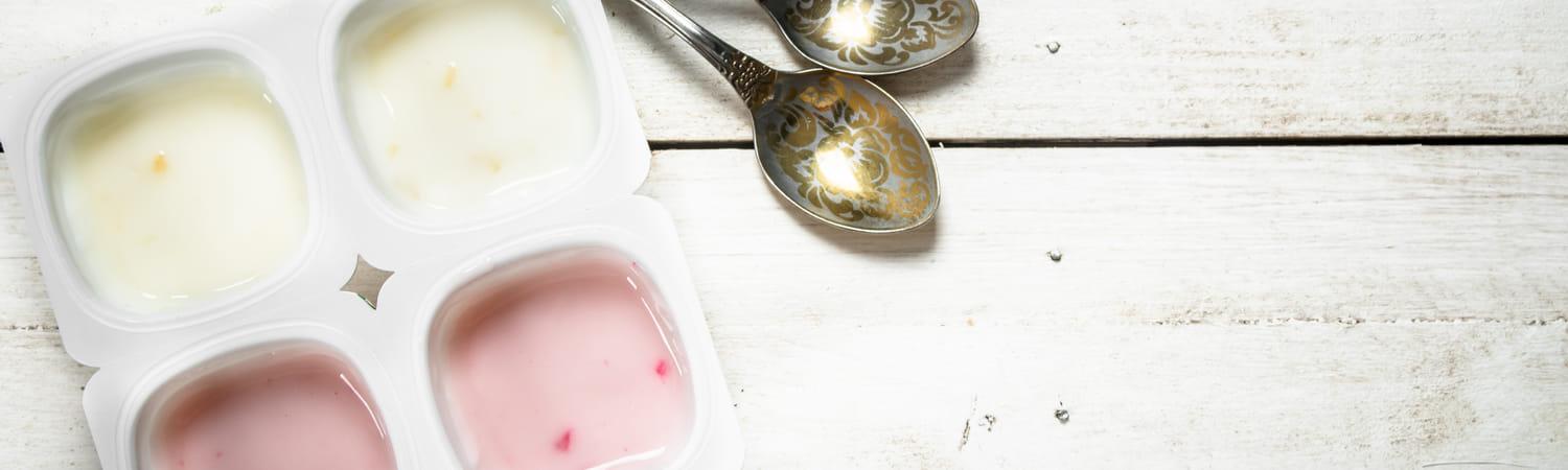 Yoghurt in plastic bakkjes, met 2 lepels ernaast.