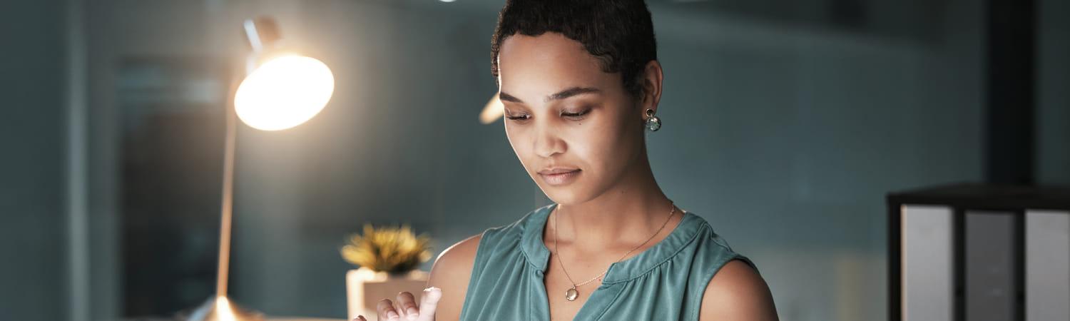 Vrouw zit met bureaulamp aan op haar tablet te werken.