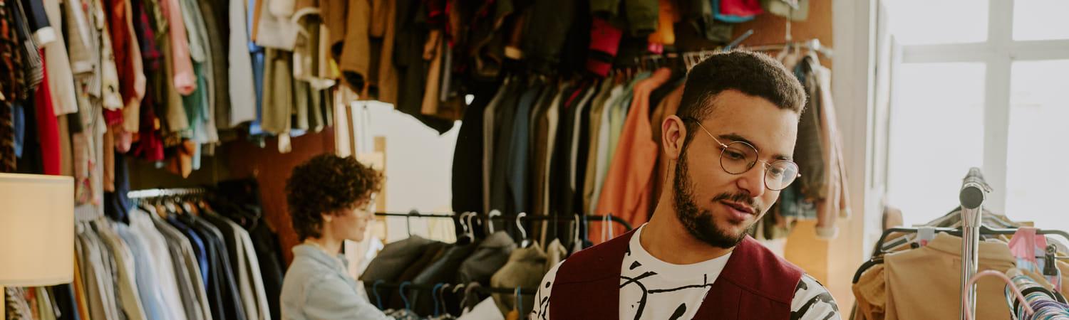 Man winkelt in een vintagewinkel en heeft tweedehands kleding vast.