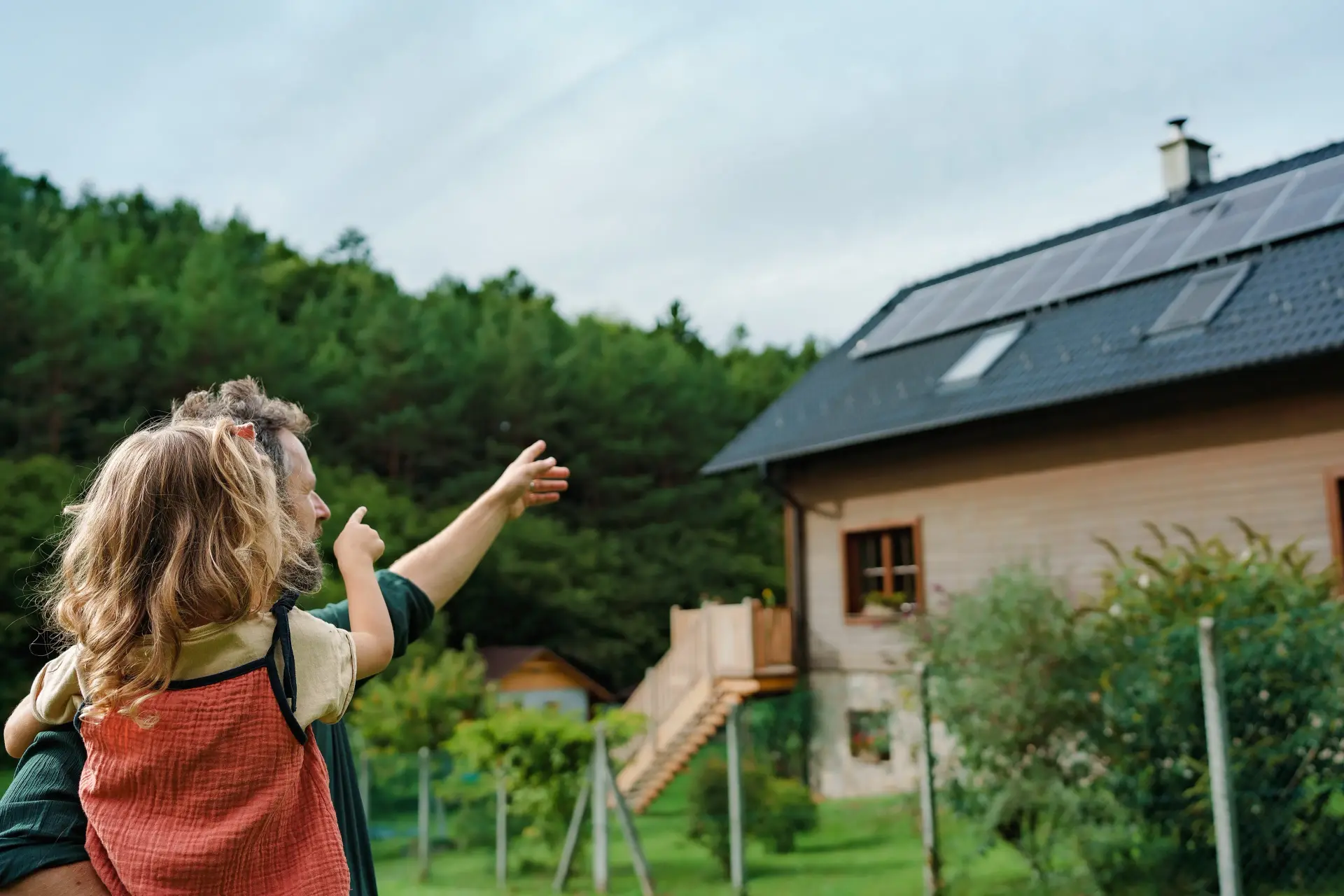 Vader met dochter op de arm wijst naar de zonnepanelen op de dak van hun huis.