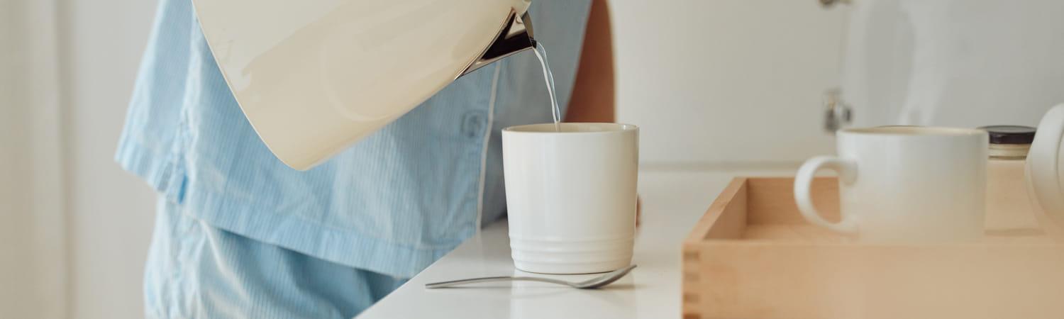 Vrouw die water uit de waterkoker in een mok giet.