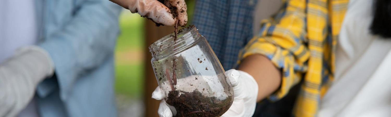 Compost wordt in een glazen potje gestopt.