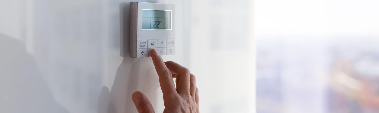 Een mannenhand stelt de verwarming in via een paneel op de wand.