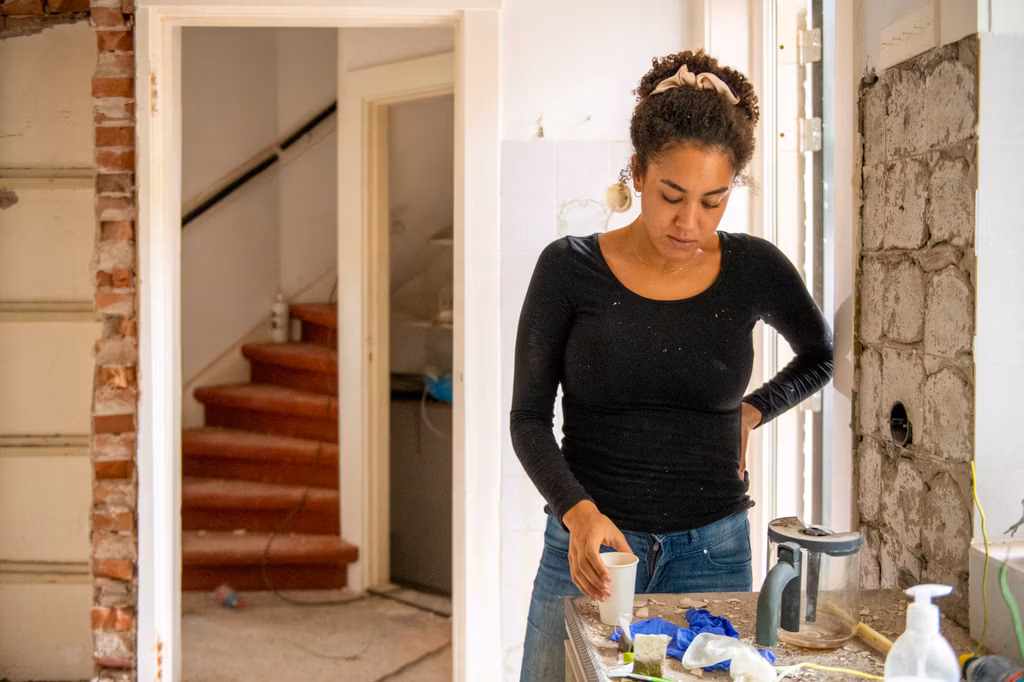 Vrouw staat in een klushuis en komt bij met een kop koffie.