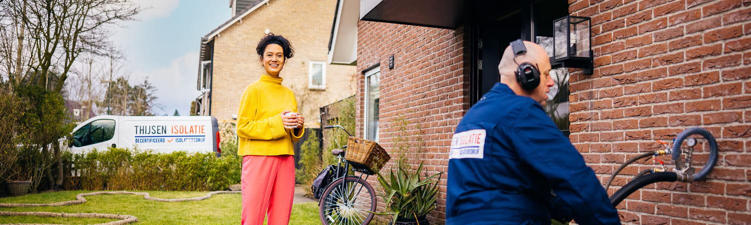 Vrolijke vrouw kijkt toe hoe een man de buitenmuur aan het isoleren is.