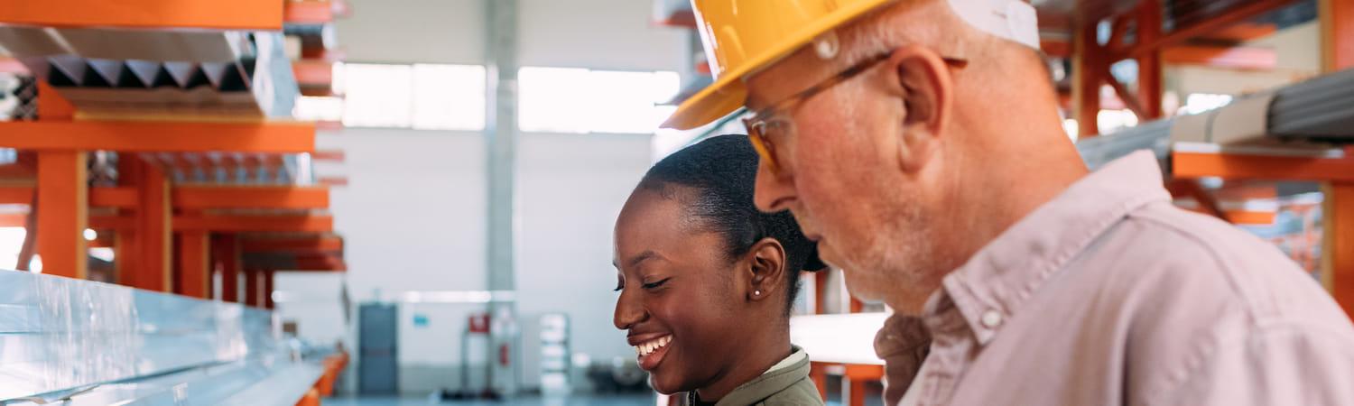 Vrouw en man hebben werkoverleg in een fabriek met oranje stellages.