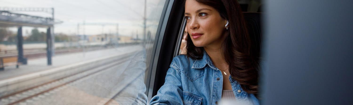 Vrouw reist met het openbaar vervoer naar werk. Ze kijkt naar buiten en luistert naar muziek.