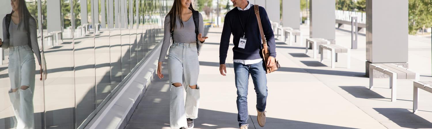 Twee mensen lopen op een trottoir en zijn in gesprek.