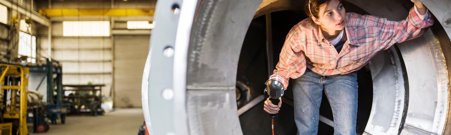 Vrouw in een fabriek loopt door een tunnelvormig voorwerp en inspecteert.