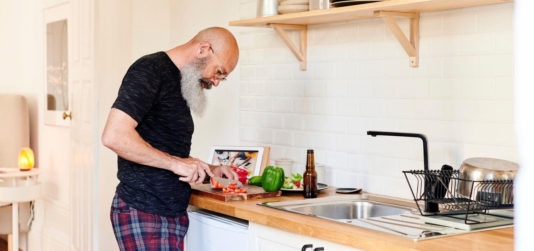Man met lange baard staat in de keuken en snijdt groente.