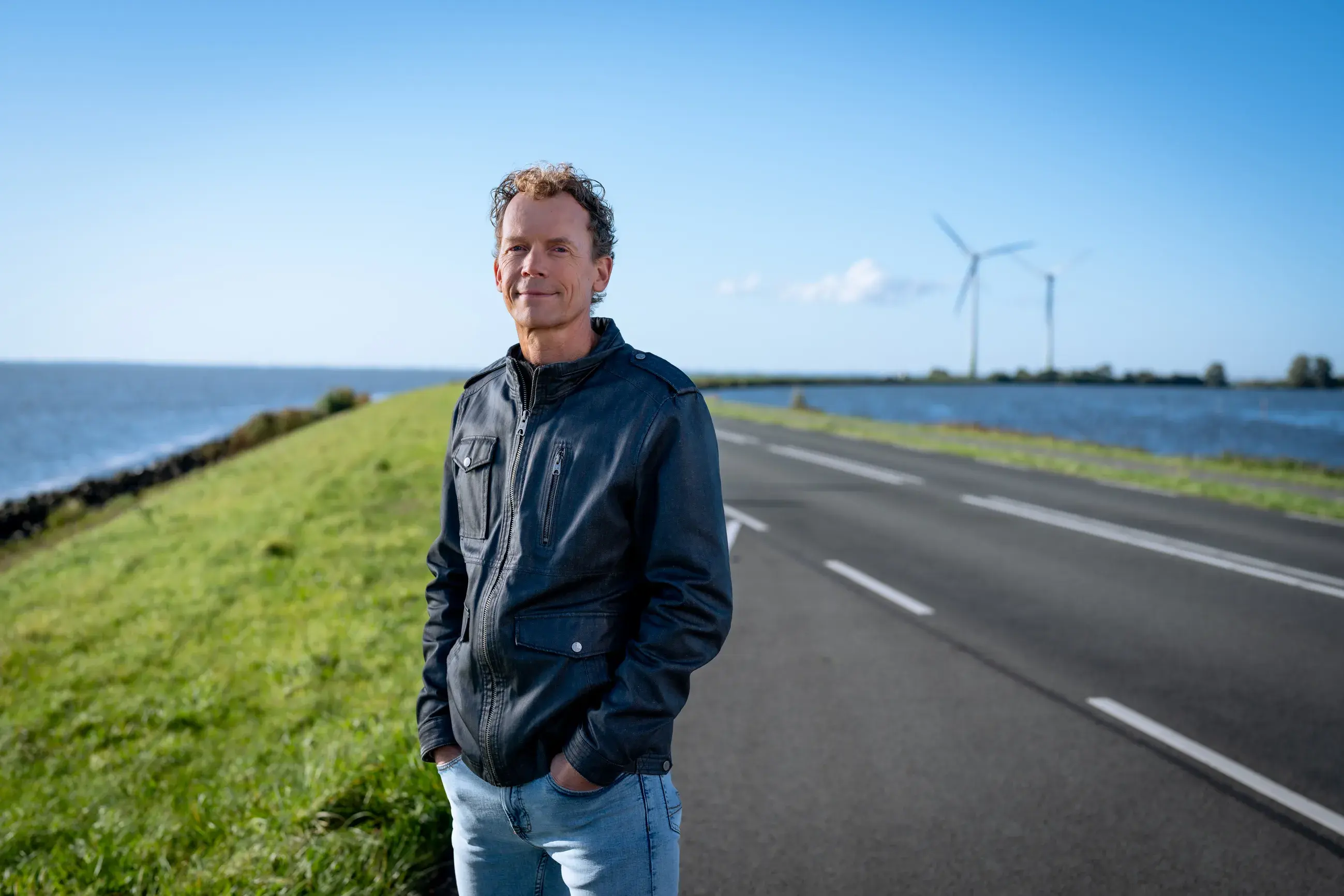 Een meneer staat op de dijk met water op de achtergrond.